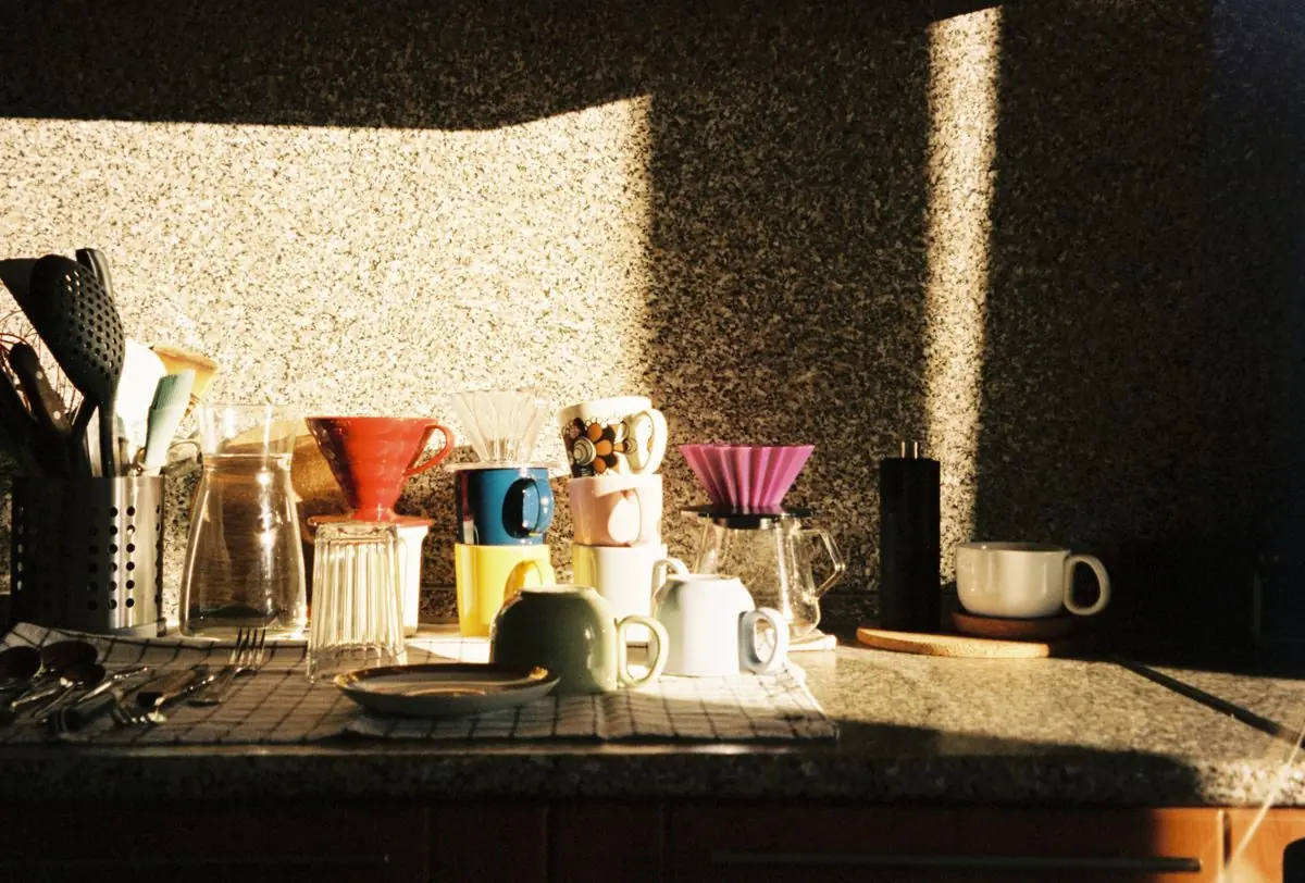 Morning sunlight on a kitchen counter with coffee mugs, a pour-over dripper and a grinder